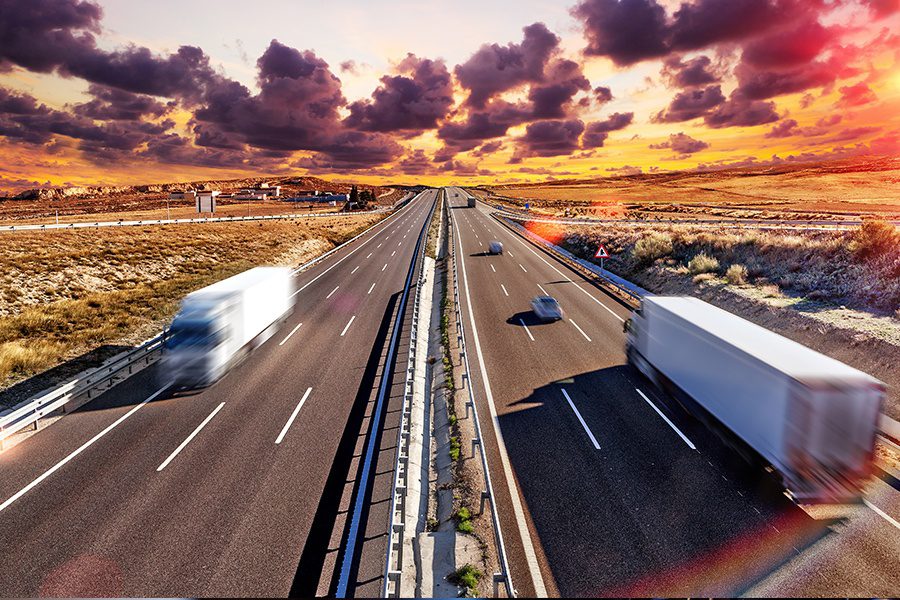 Transportation Insurance - Blurred View of a Long Stretch of Highway with Trucks and Cars Traveling in Both Directions at Dusk