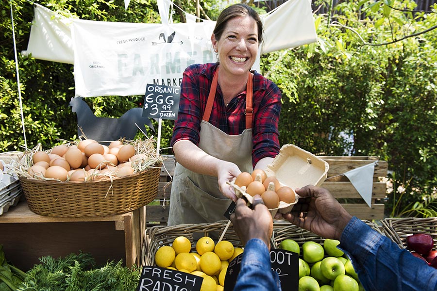 Business Insurance - Woman Selling Her Produce at a Farmers Market Stand, Smiling and Wearing Apron