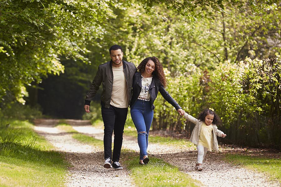 Personal Insurance - Mother, Father and Young Daughter Walking Down a Path in a Green Park